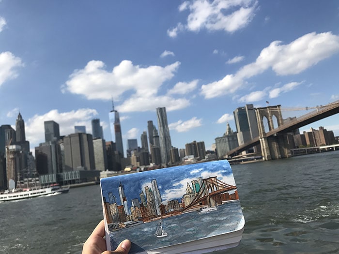 Picture of a sketchbook study of the NYC skyline held in front of skyline reference